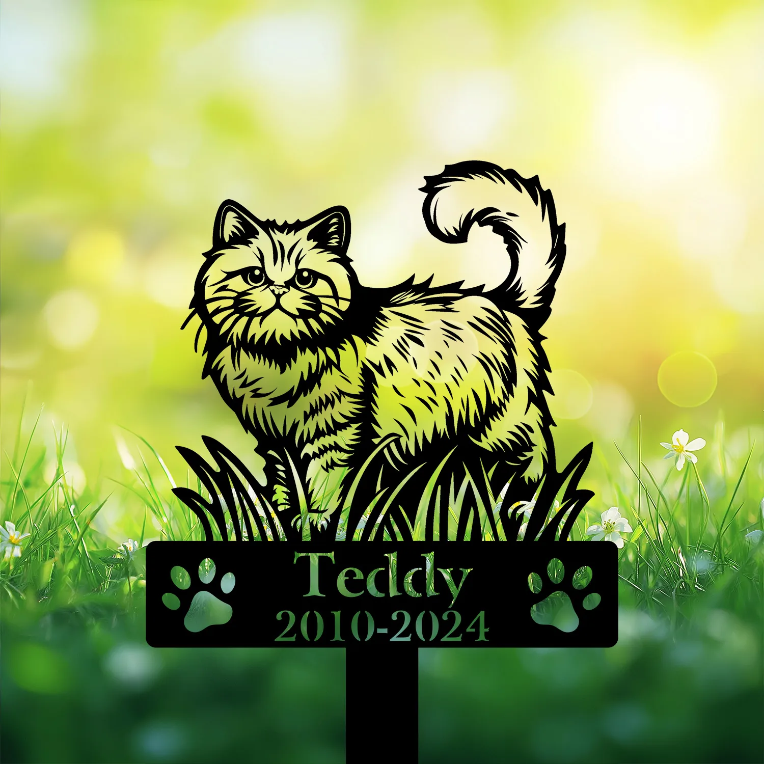 Black cat memorial garden stake reading “Teddy 2010-2024” with paw prints, displayed in grass with flowers