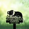 Black dog memorial garden stake in grass with daisies, reading “In Loving Memory Of Cooper 2012-2024”