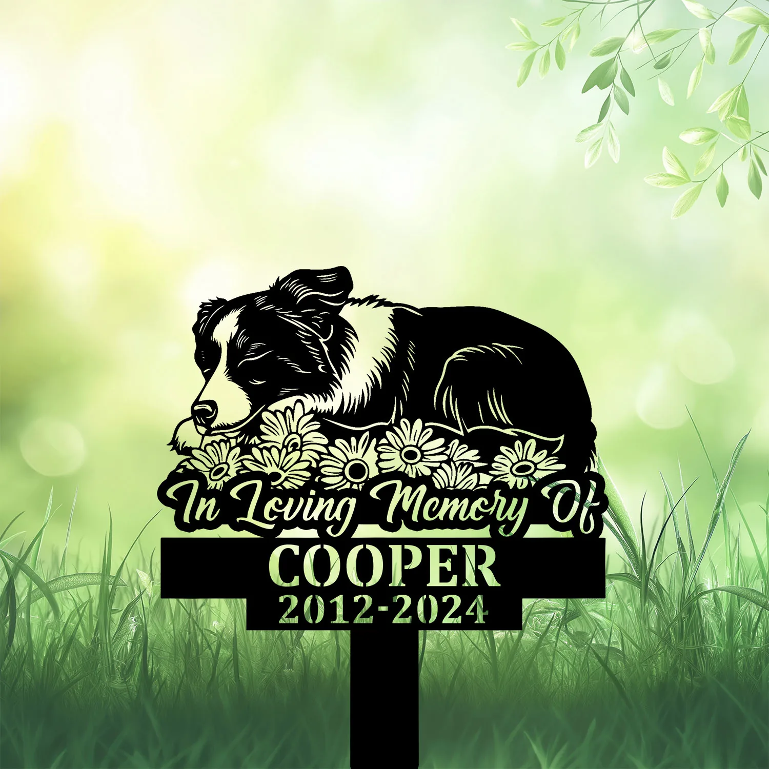 Black dog memorial garden stake in grass with daisies, reading “In Loving Memory Of Cooper 2012-2024”