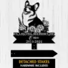 A black metal memorial sign featuring a corgi, flowers, and text 'In Loving Memory of Orion 2014-2024', with detached stakes.
