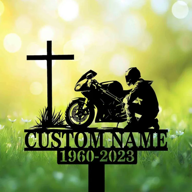 A silhouette memorial featuring a cross, a motorcycle, and a kneeling figure, with a custom name and dates.