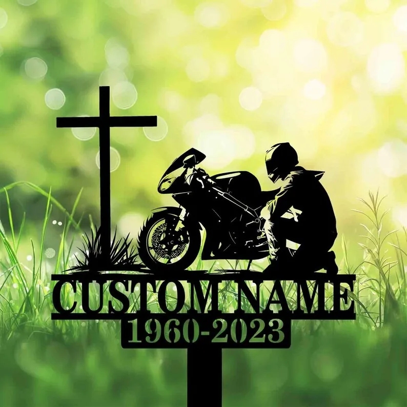 A silhouette design featuring a motorcycle and a rider beside a cross, set against a blurred green background.
