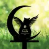 A silhouette of a cat with wings on a crescent moon, set against a blurred green background.