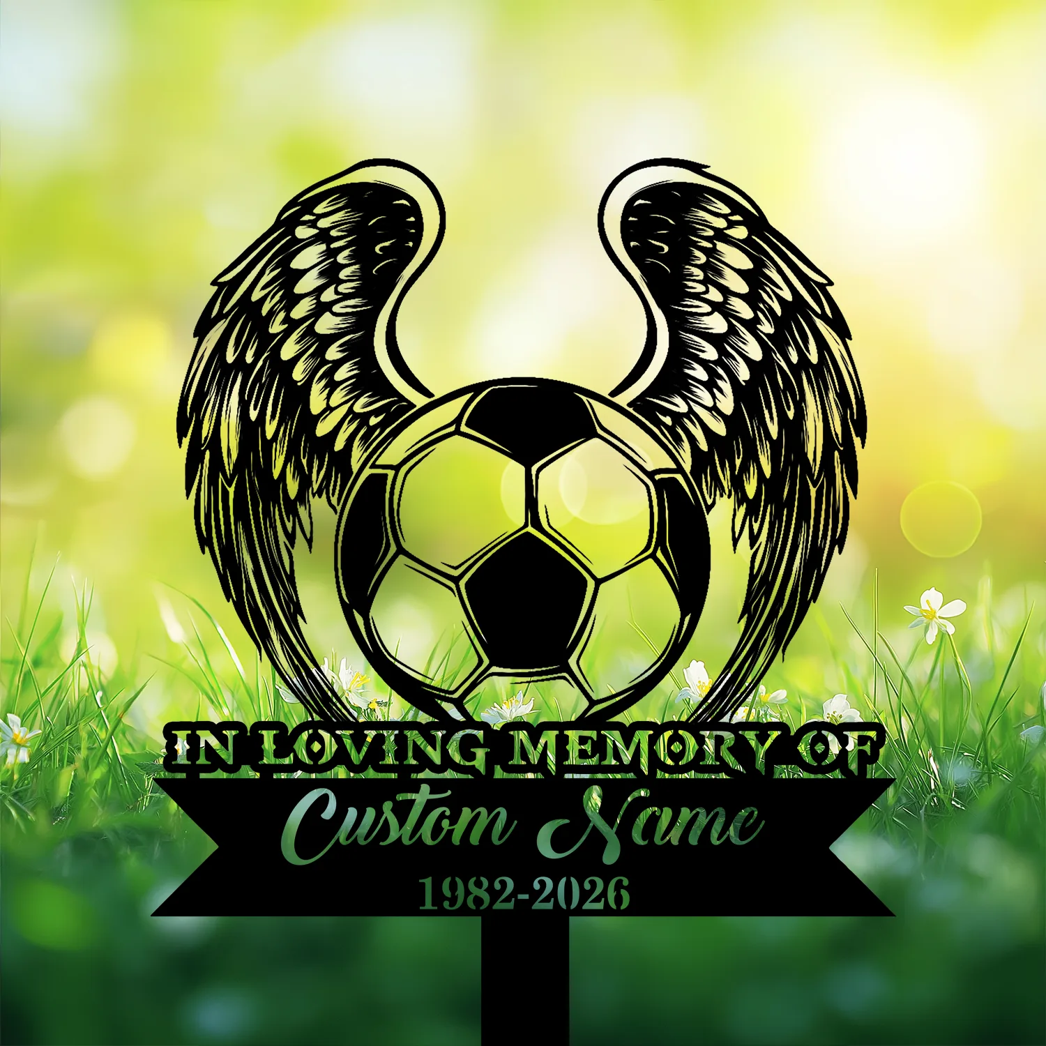 Black silhouette memorial sign with angel wings around a soccer ball over a grass field, text reads "IN LOVING MEMORY OF" and placeholder "Custom Name" with dates 1982-2026
