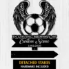 Black metal memorial sign showing a soccer ball with angel wings, banner reading "In Loving Memory of Custom Name" and dates 1982-2026 on a light wood background