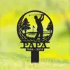 Black metal grave or garden stake shaped like a golf ball silhouette with a golfer swinging, trees, flag, and the text "PAPA 1944 - 2025" against a blurred green background