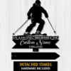 Black metal memorial sign showing a skier silhouette above text reading "In Loving Memory of Custom Name 1986-2026" on a light wood background