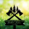 Black memorial sign with crossed axes and pine tree silhouettes reading "In Loving Memory" and "Custom Name 1982-2026" against sunlit grassy background