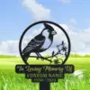 Black metal memorial garden sign featuring a perched cardinal on a branch with flowers and engraved text 'In Loving Memory Of CUSTOM NAME 1950 - 2024' against a grassy field and blue sky