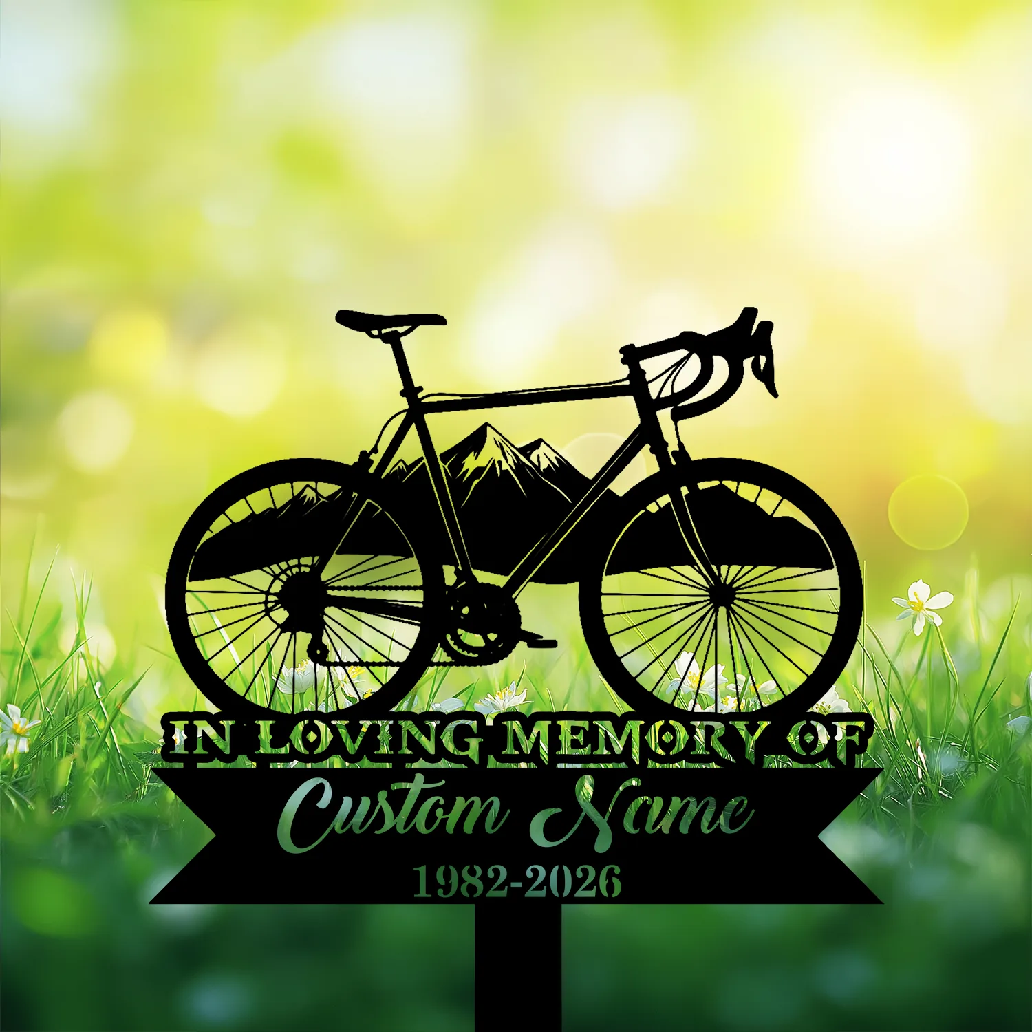 Black silhouette of a road bicycle over a ribbon sign reading "In Loving Memory" and placeholder "Custom Name 1982-2026" against a sunlit grassy background