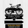 Black metal memorial sign shaped like a bicycle over mountains with text "In Loving Memory of Custom Name 1982-2026" on a white wood background