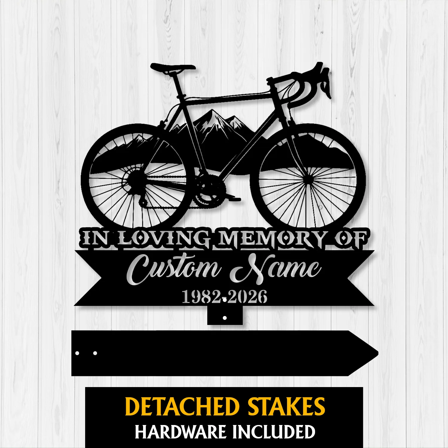Black metal memorial sign shaped like a bicycle over mountains with text "In Loving Memory of Custom Name 1982-2026" on a white wood background