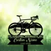 Black silhouette memorial sign of a road bicycle over mountain graphic and ribbon reading "In Loving Memory" and "Custom Name 1982-2026" on a soft green grassy background