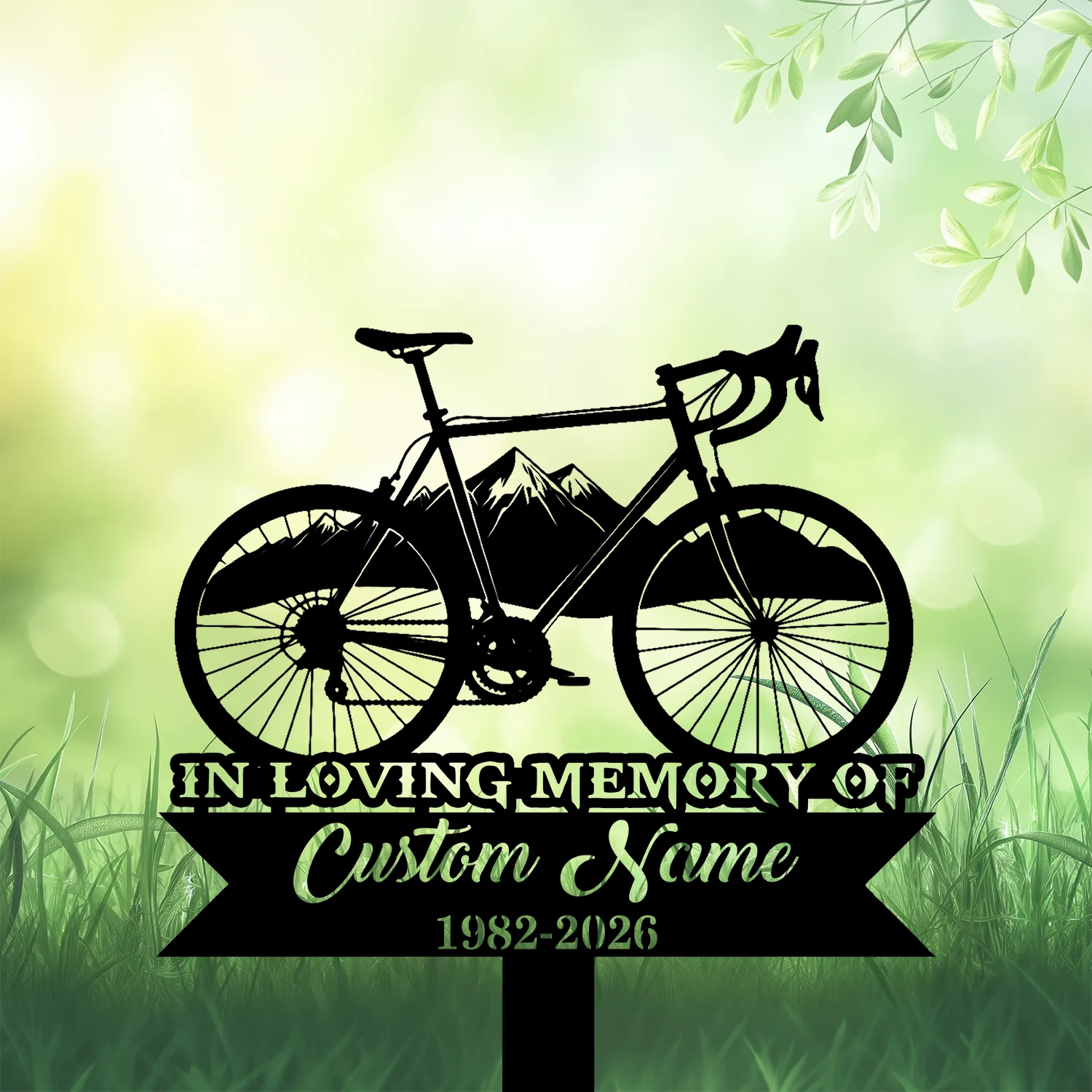 Black silhouette memorial sign of a road bicycle over mountain graphic and ribbon reading "In Loving Memory" and "Custom Name 1982-2026" on a soft green grassy background