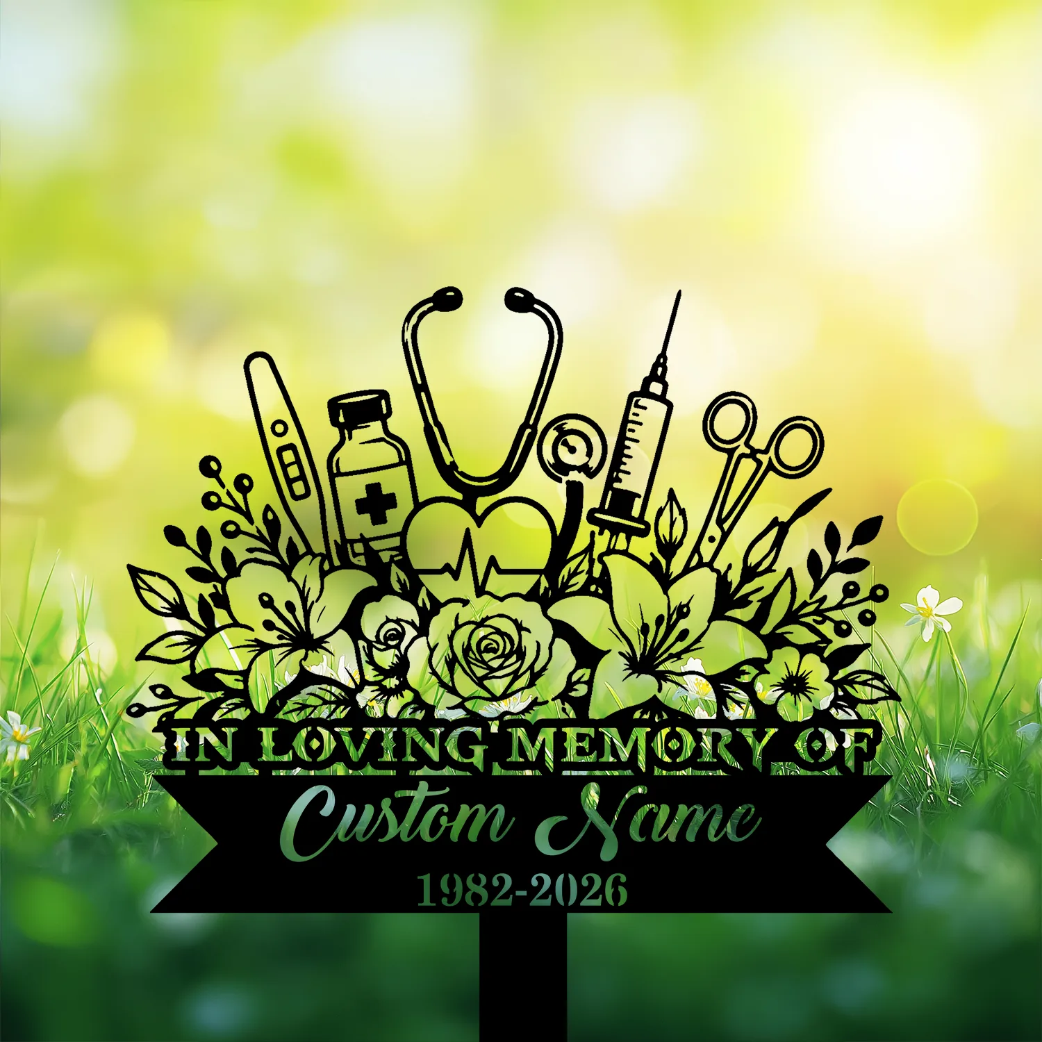 Black memorial garden sign with flowers and medical icons (stethoscope, syringe, vial, thermometers) reading "IN LOVING MEMORY" and placeholder "Custom Name 1982-2026" against a sunlit grassy background