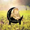 Cute sleeping baby angel with halo and wings sitting on a black crescent moon sign in a grassy outdoor setting, text reading "I love you to the moon" and placeholder "CUSTOM NAME"