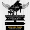 Black silhouette memorial sign of a grand piano with angel wings above a banner reading “In Loving Memory of” and placeholder “Custom Name” with years 1982–2026 on a light wood background