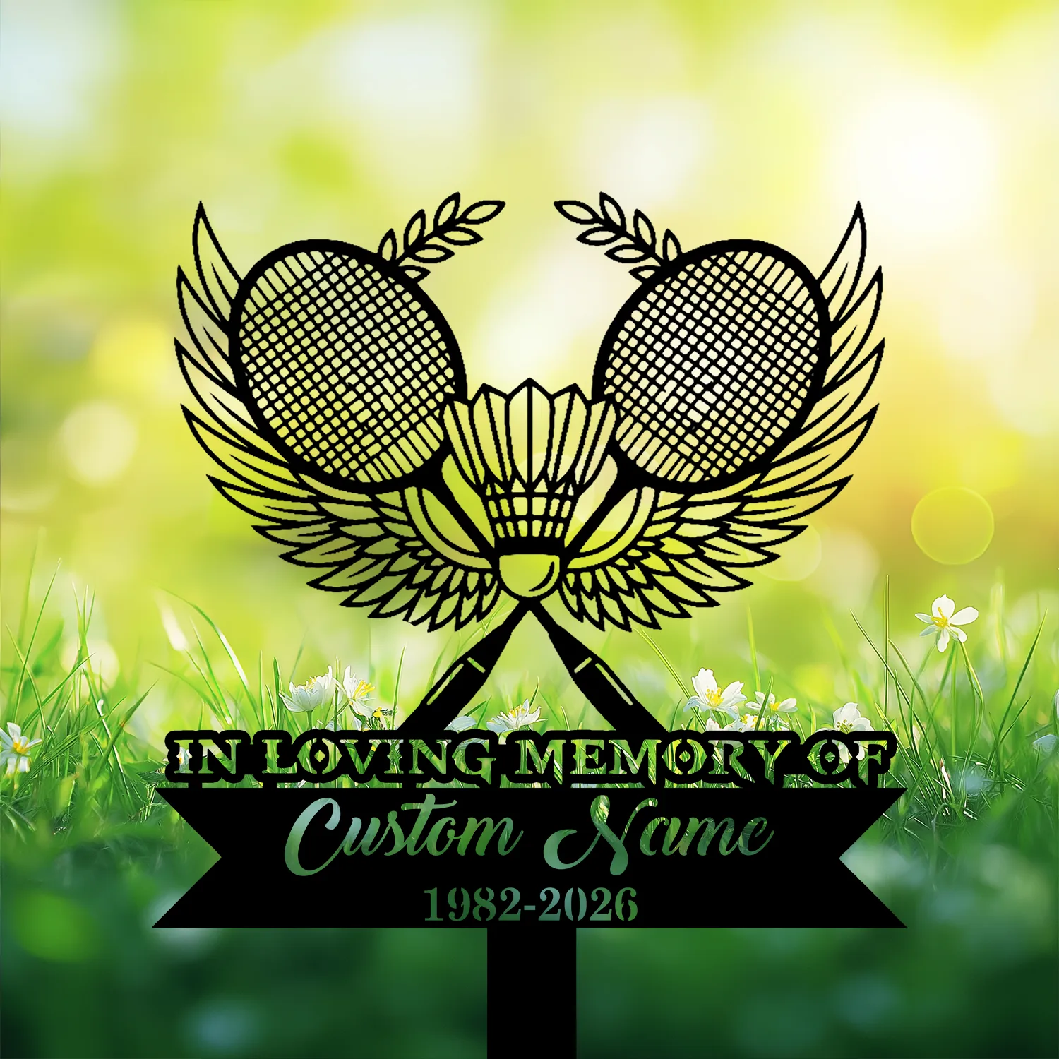 3-3 Black memorial sign with crossed badminton rackets, shuttlecock and wings above text reading "In Loving Memory of Custom Name 1982-2026" set against a sunlit grassy background with small white flowers