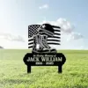 Black memorial lawn sign with American flag, combat boots and helmet, reading "In Loving Memory of JACK WILLIAM 1956 - 2025," placed on green grass under a partly cloudy sky