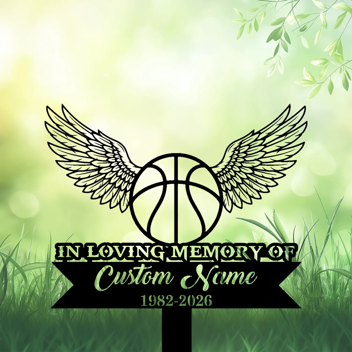 4b-3 Memorial sign with a basketball and angel wings above grass, text reads "In Loving Memory of" and placeholder "Custom Name" with years 1982-2026 on a soft green leafy background
