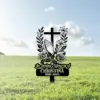 Black memorial yard sign with cross, praying hands and roses reading 'In Loving Memory of CHRISTINA 1980-2025' placed in grassy field under blue sky