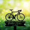 6-3 Black silhouette memorial sign of a road bicycle over grass and flowers with text placeholders "IN LOVING MEMORY OF", "Custom Name" and dates "1982-2026" against a sunny bokeh background
