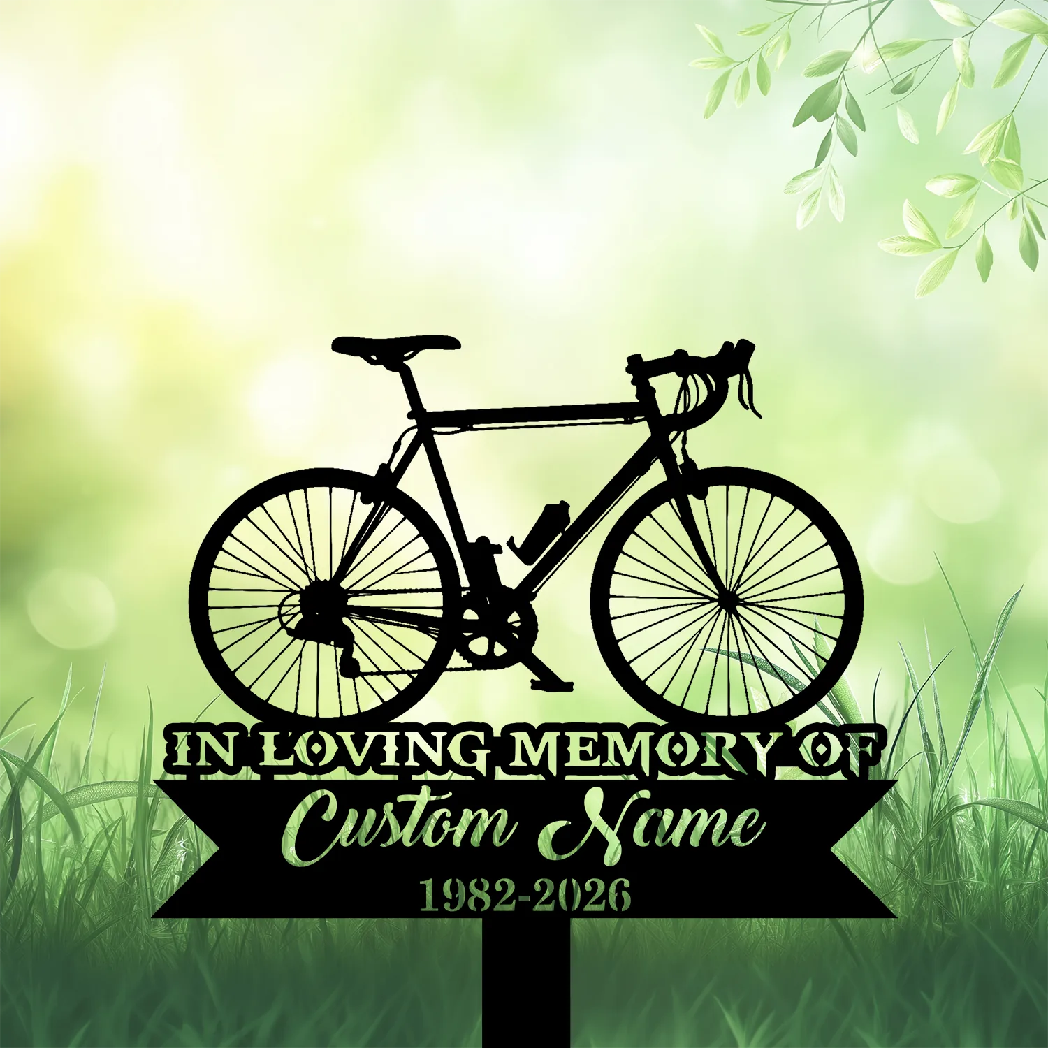 6b-3 Black silhouette of a road bicycle above a memorial sign reading "In Loving Memory" with placeholder "Custom Name" and dates 1982-2026, set against a soft green grassy background