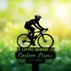 Silhouette of a cyclist on a memorial sign reading "In Loving Memory of" and "Custom Name 1987-2026" against a sunny grassy background with flowers