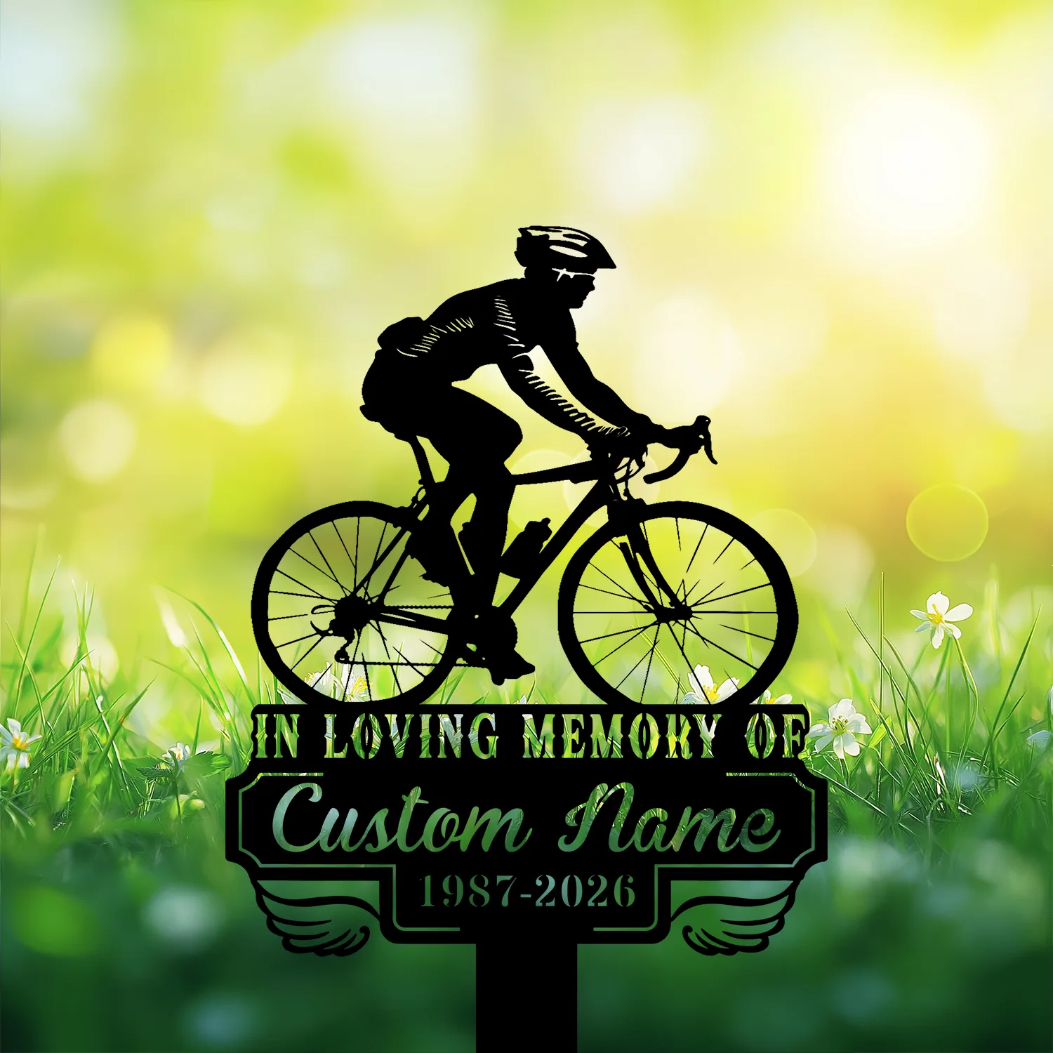 Silhouette of a cyclist on a memorial sign reading "In Loving Memory of" and "Custom Name 1987-2026" against a sunny grassy background with flowers