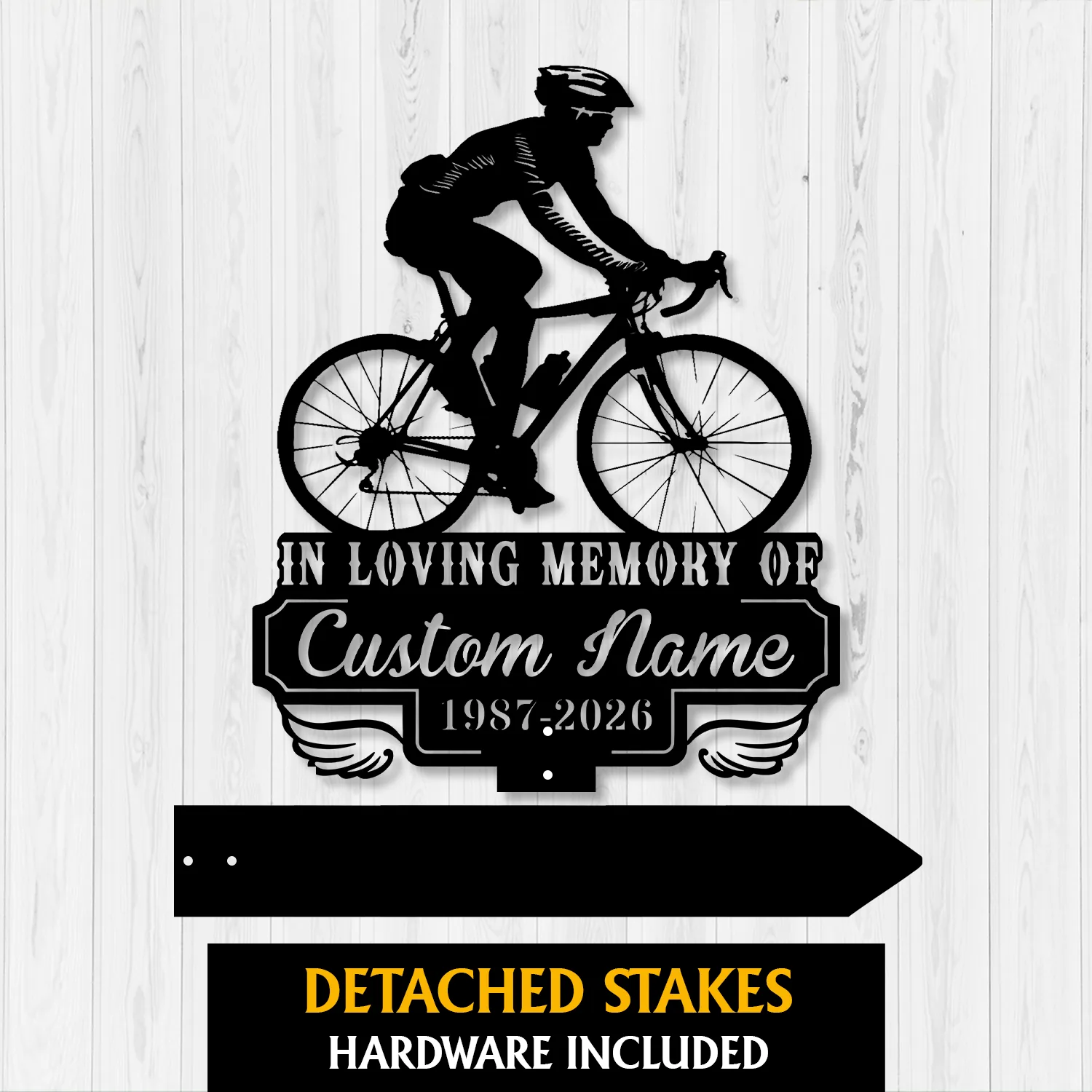 Black metal memorial sign showing a cyclist silhouette above text reading "In Loving Memory of Custom Name 1987-2026" on a pale wood background
