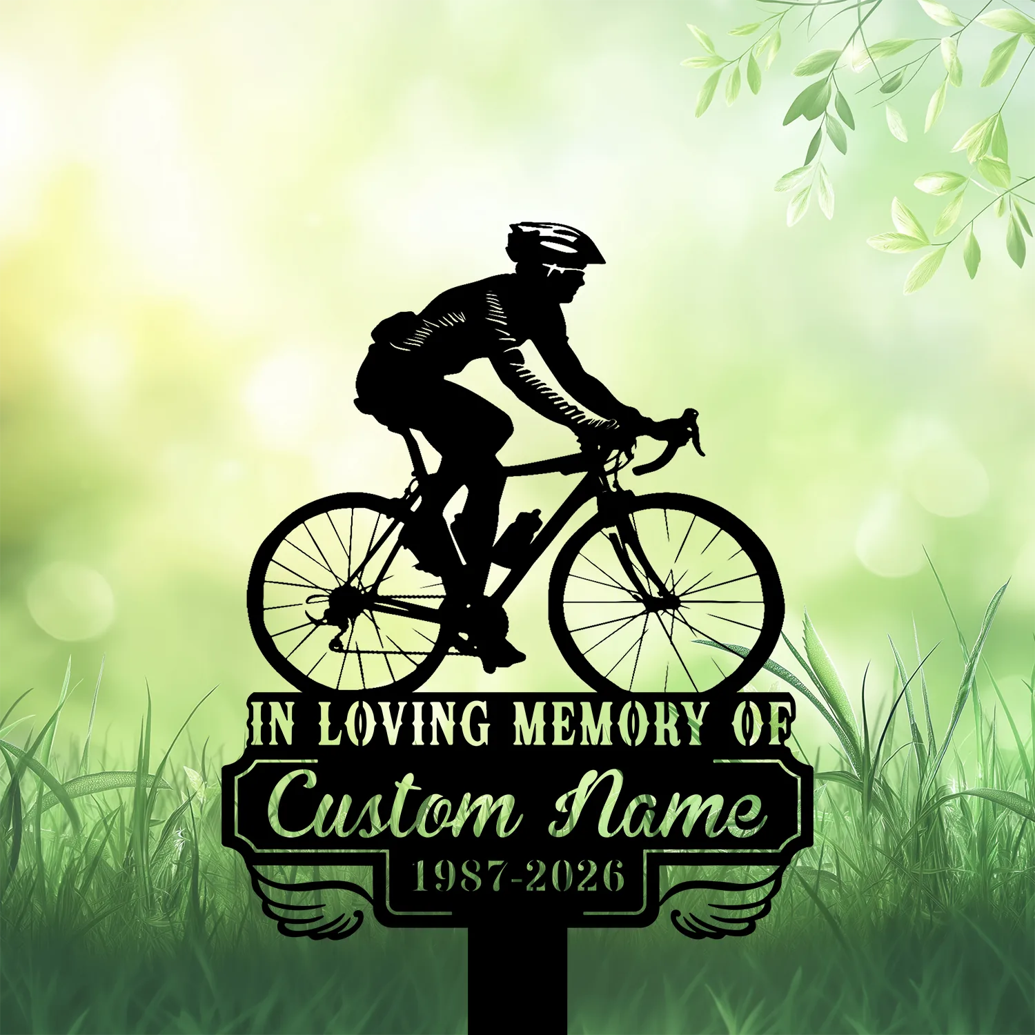 Silhouette of a cyclist on a road bike above a memorial plaque reading "IN LOVING MEMORY OF" and placeholder "Custom Name 1987-2026" on a grassy green background
