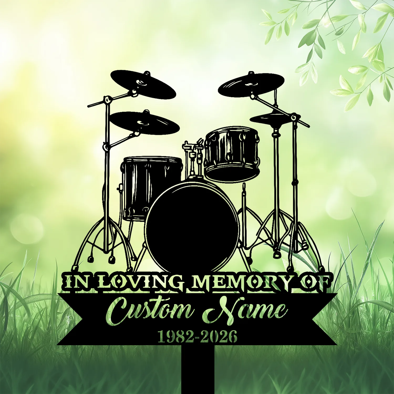 7b-3 Black silhouette of a drum kit memorial sign reading "In Loving Memory of" with placeholder "Custom Name" and dates 1982–2026 on a green grassy, leafy background