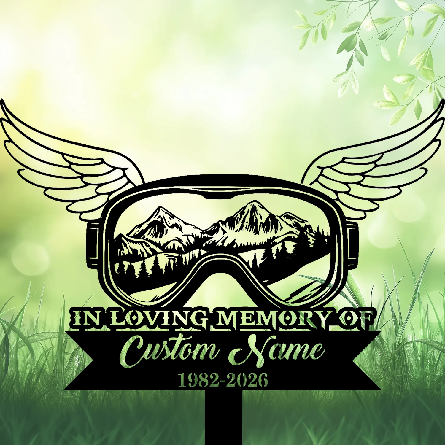 7b-4 Black memorial sign with winged ski goggles showing mountain scene, text "IN LOVING MEMORY OF" and placeholder "Custom Name 1982-2026" on a soft green grassy background