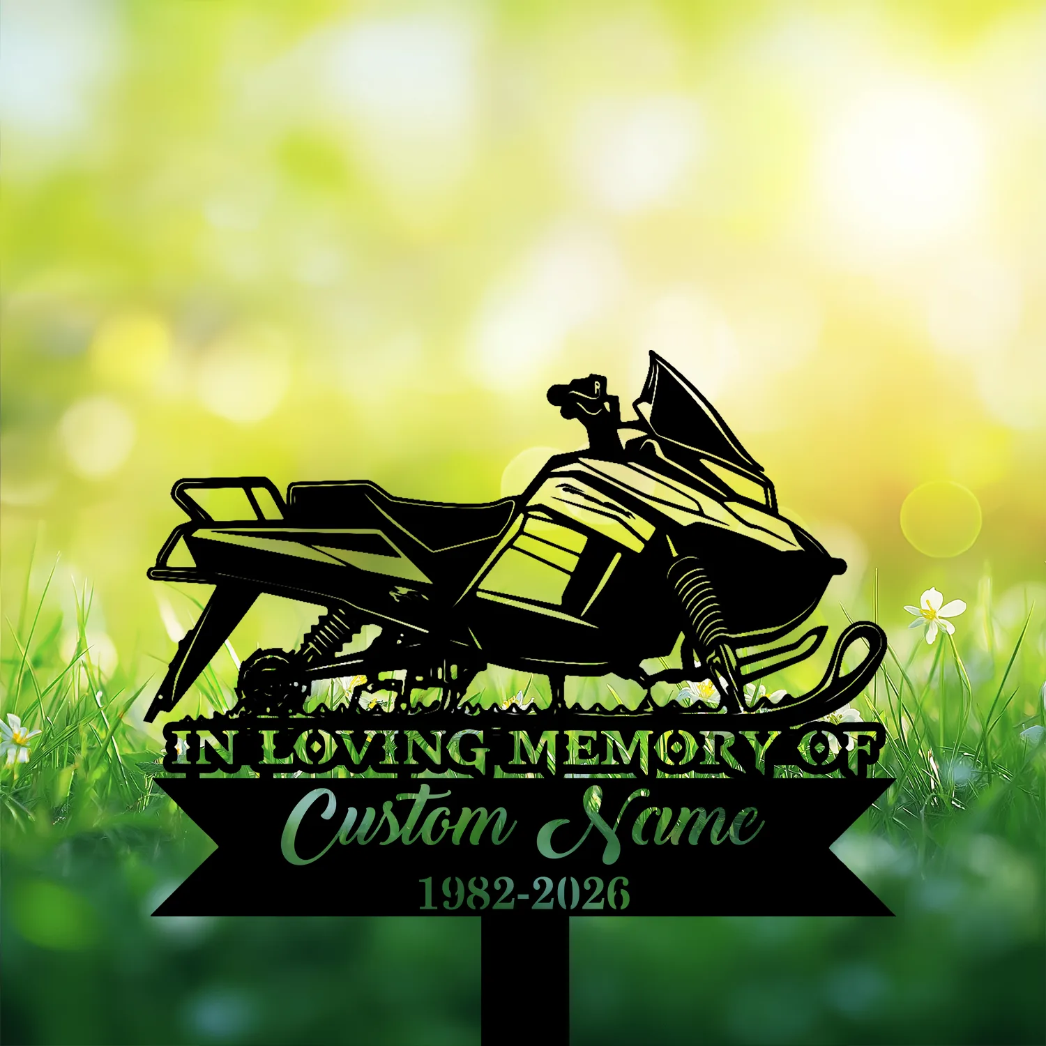 8-3 Black silhouette memorial sign of a snowmobile reading "IN LOVING MEMORY OF" with placeholder "Custom Name" and dates "1982-2026" set against sunlit green grass and bokeh background