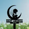 Black silhouette garden stake of a winged baby sitting on a crescent moon with text "BABY ANDREA" and year "2026" against a blue sky and dandelion field