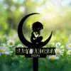 Black silhouette cake topper of a winged baby sitting on a crescent moon with text 'BABY ANDREA 2026' over a blurred daisy field background