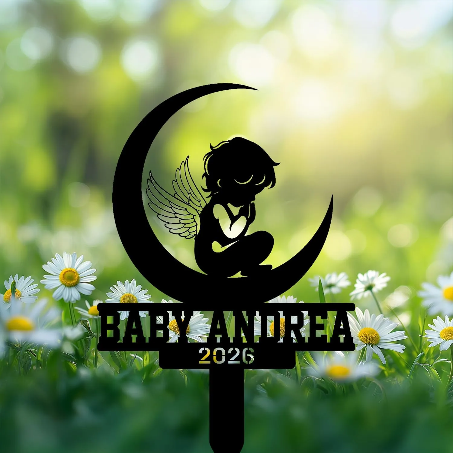 Black silhouette cake topper of a winged baby sitting on a crescent moon with text 'BABY ANDREA 2026' over a blurred daisy field background