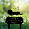 Black silhouette lawn memorial sign of a sleeping baby with angel wings on a cloud, daisies and blurred green garden background, text reading "I'll hold you in my heart until I can hold you in heaven 2026"