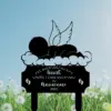 Black silhouette memorial lawn stake showing a sleeping angel baby on clouds with wings and text “I’ll hold you in my heart until I can hold you in heaven 2026,” set against blue sky and dandelion field