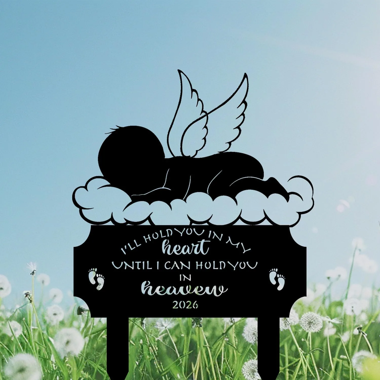 Black silhouette memorial lawn stake showing a sleeping angel baby on clouds with wings and text “I’ll hold you in my heart until I can hold you in heaven 2026,” set against blue sky and dandelion field