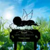 Black silhouette lawn memorial sign showing a sleeping baby with angel wings on a cloud, text cutout reading "I'll hold you in my heart until I can hold you in heaven 2026", set in grassy field with blue sky and wildflowers