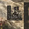 Black metal address plaque mounted on a brick exterior showing numbers 1565 and text "FAIRWAY DRIVE" with a sitting dog, flowers and butterflies