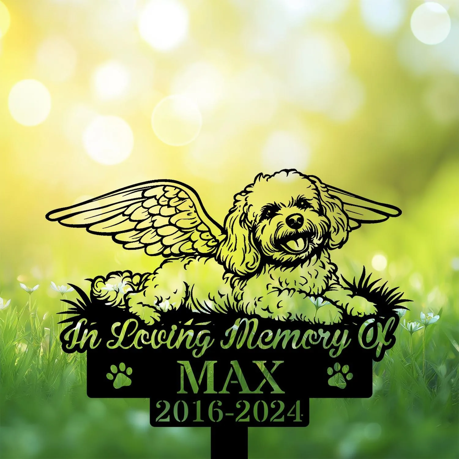 Black silhouette memorial sign of a small fluffy dog with angel wings lying on grass, text "In Loving Memory Of" above and "MAX 2016-2024" below on a sunny bokeh background