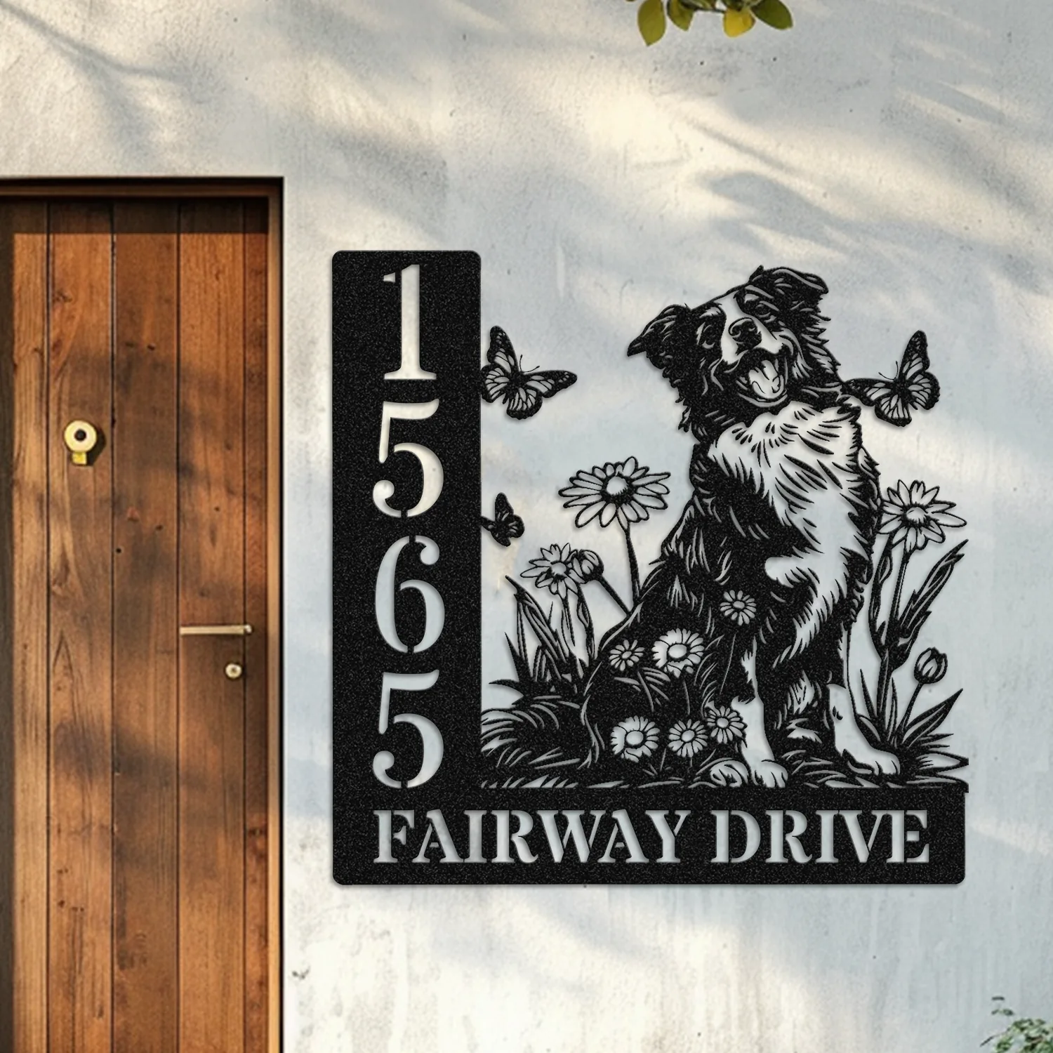 Border-Collie-Sitting-with-Butterfly-1 Black metal house sign mounted on a pale exterior wall beside a wooden door, showing vertical address numbers 1565 and “FAIRWAY DRIVE” with a decorative dog, flowers and butterflies design