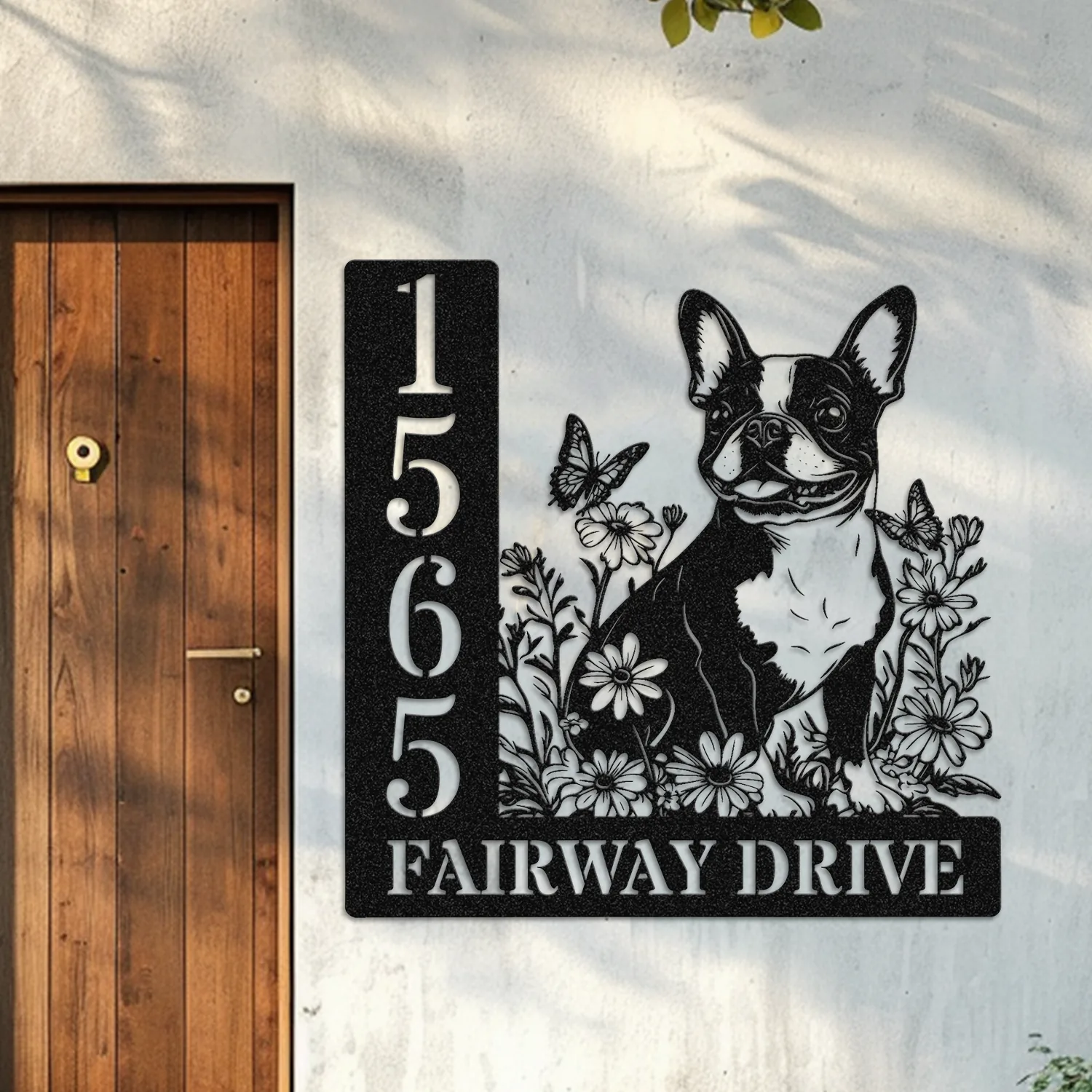 Boston-Terrier-Sitting-with-Butterfly-1-2 black metal house sign mounted next to a wooden door showing numbers 15655 and text 'FAIRWAY DRIVE' with a floral design and a happy French bulldog silhouette