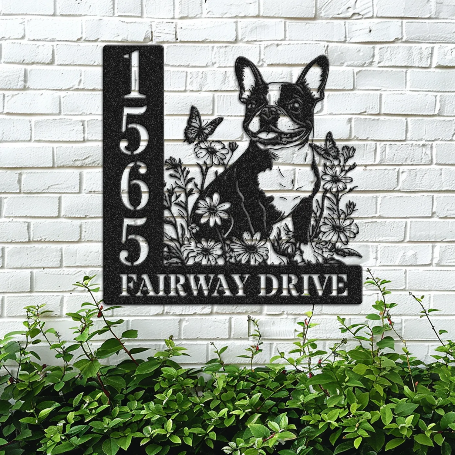Boston-Terrier-Sitting-with-Butterfly-3 Black metal house sign on a white brick wall showing numbers 1565 and the text FAIRWAY DRIVE with a dog silhouette surrounded by flowers and butterflies above green shrubs