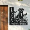 Black metal house sign mounted next to a wooden door showing numbers 1565 and text "Fairway Drive" with a decorative dog, flowers, and butterflies on a white stucco wall