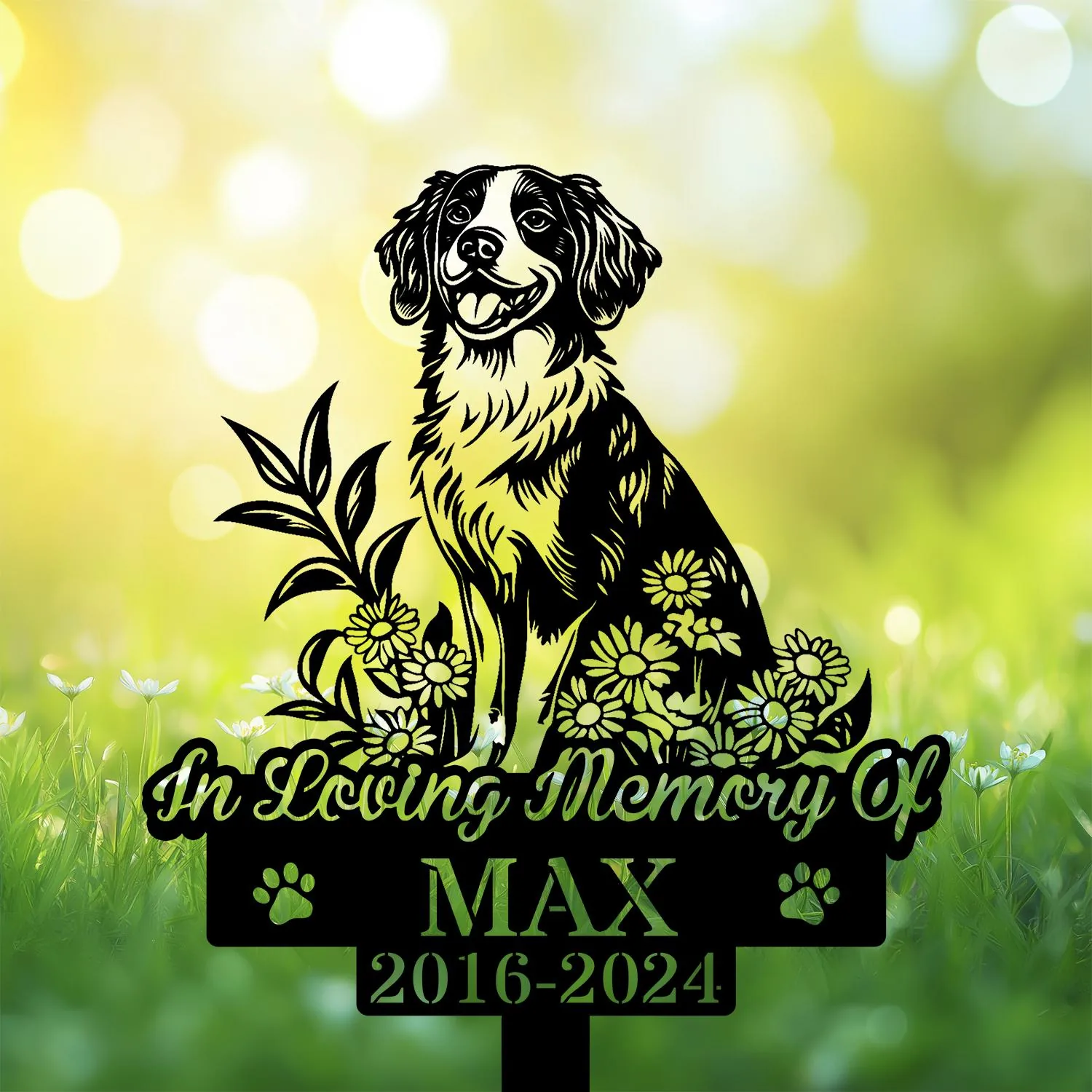 Black silhouette memorial garden stake of a happy dog surrounded by flowers with text "In Loving Memory Of" and name "MAX" and dates 2016-2024 against a sunny green bokeh background