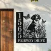 Brittany-Spaniel-Sitting-with-Butterfly-1 Black metal house sign mounted on an exterior wall next to a wooden door, showing numbers 1565, text 'FAIRWAY DRIVE', and a dog sitting among flowers with butterflies