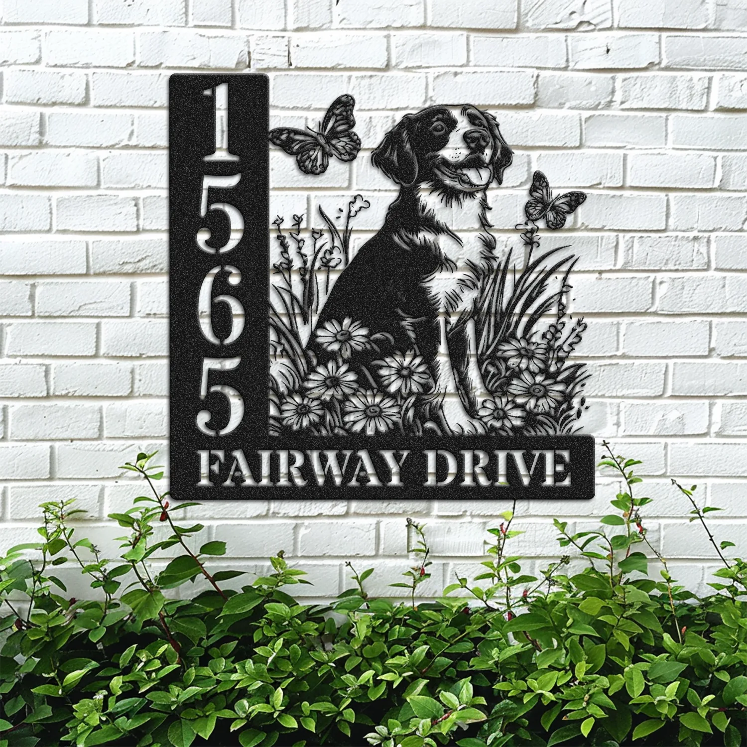 Brittany-Spaniel-Sitting-with-Butterfly-3 Black metal house sign mounted on a white brick wall showing address 1565 and the text FAIRWAY DRIVE beside a sitting dog with flowers and butterflies, greenery below